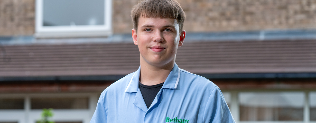 A male Health & Social Care learner pictured in a blue uniform outside his place of work